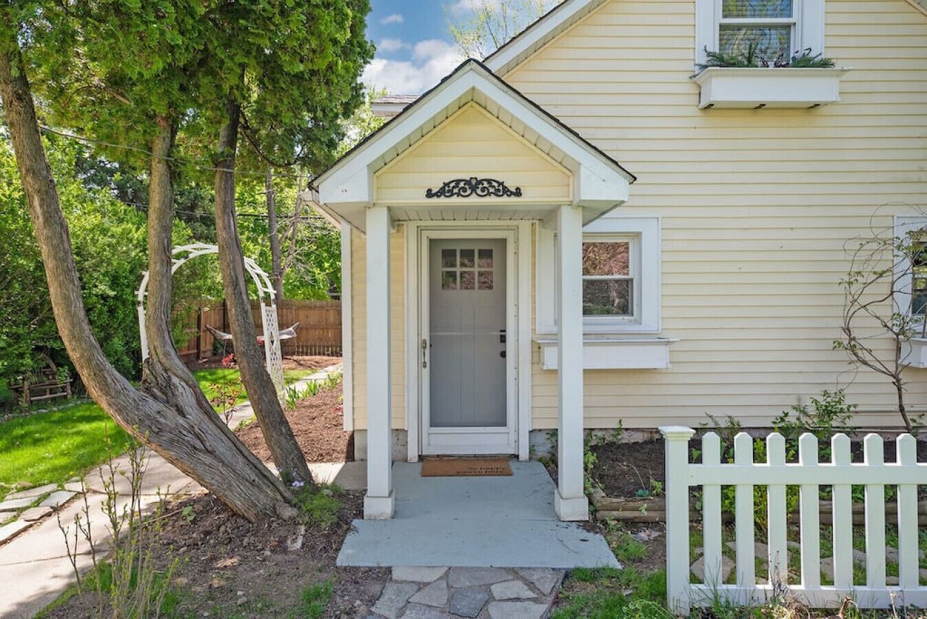 Une maison avec un porche à l’avant, une clôture blanche en bois et un jardin bien entretenu.