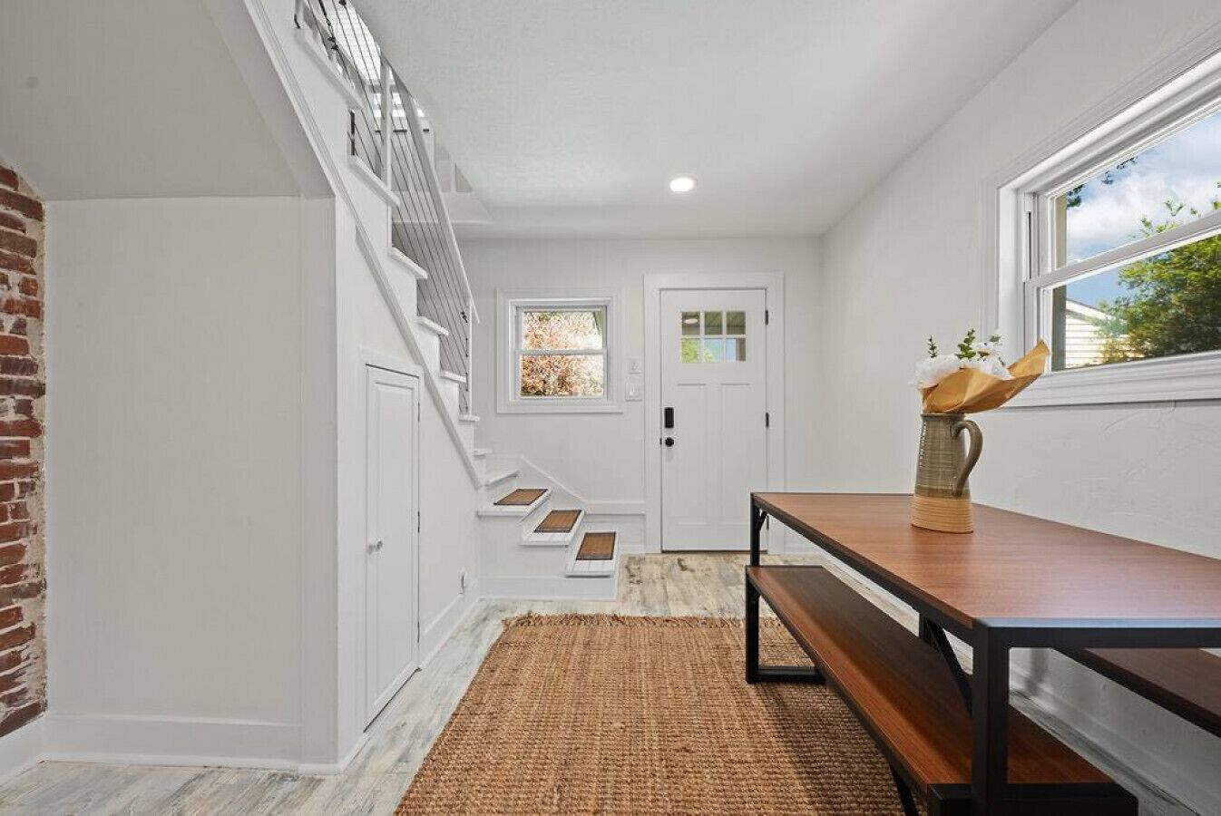 Un couloir avec un escalier, un banc en bois, un tapis et une fenêtre donnant sur des arbres.
