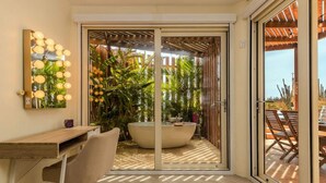 Habitación moderna con escritorio, silla y un amplio ventanal corredero que da a un área exterior con piscina y plantas tropicales.
