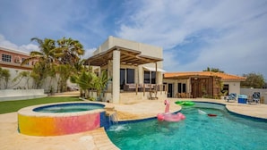 Una piscina con hidromasaje, sillas de descanso y palmeras.
