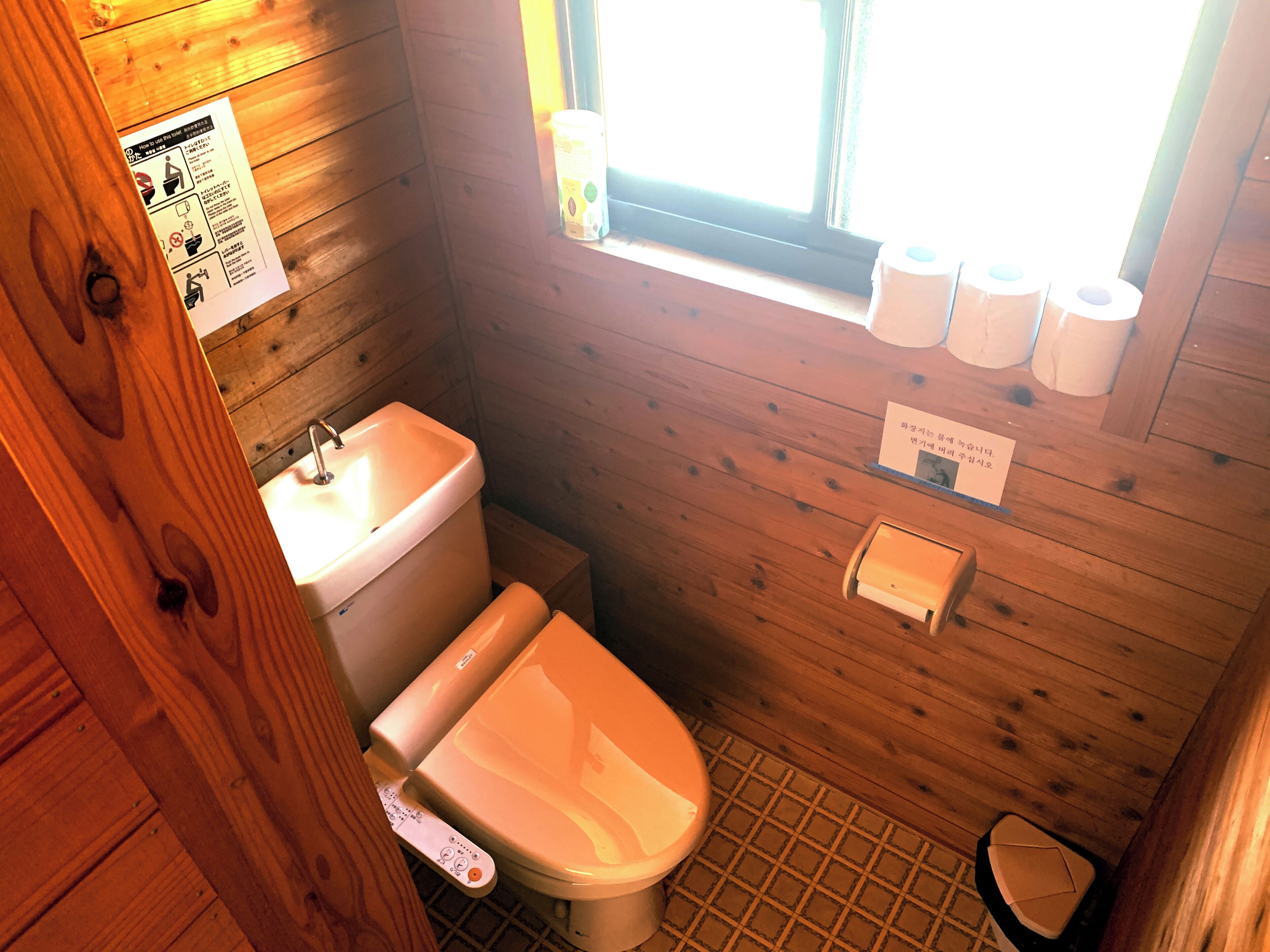 A wooden cabin bathroom with a toilet, sink, and window.