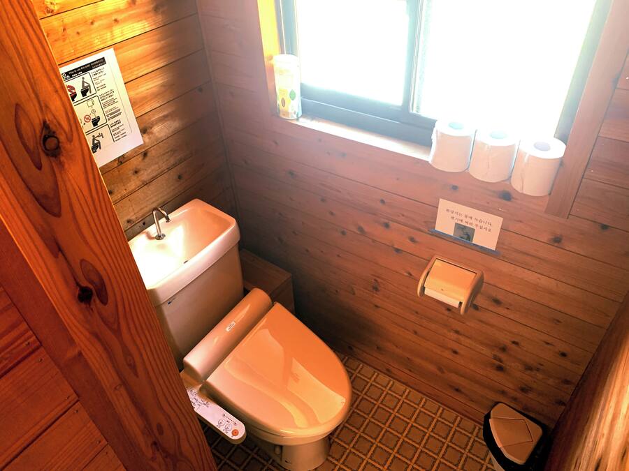 A wooden cabin bathroom with a toilet, sink, and window.
