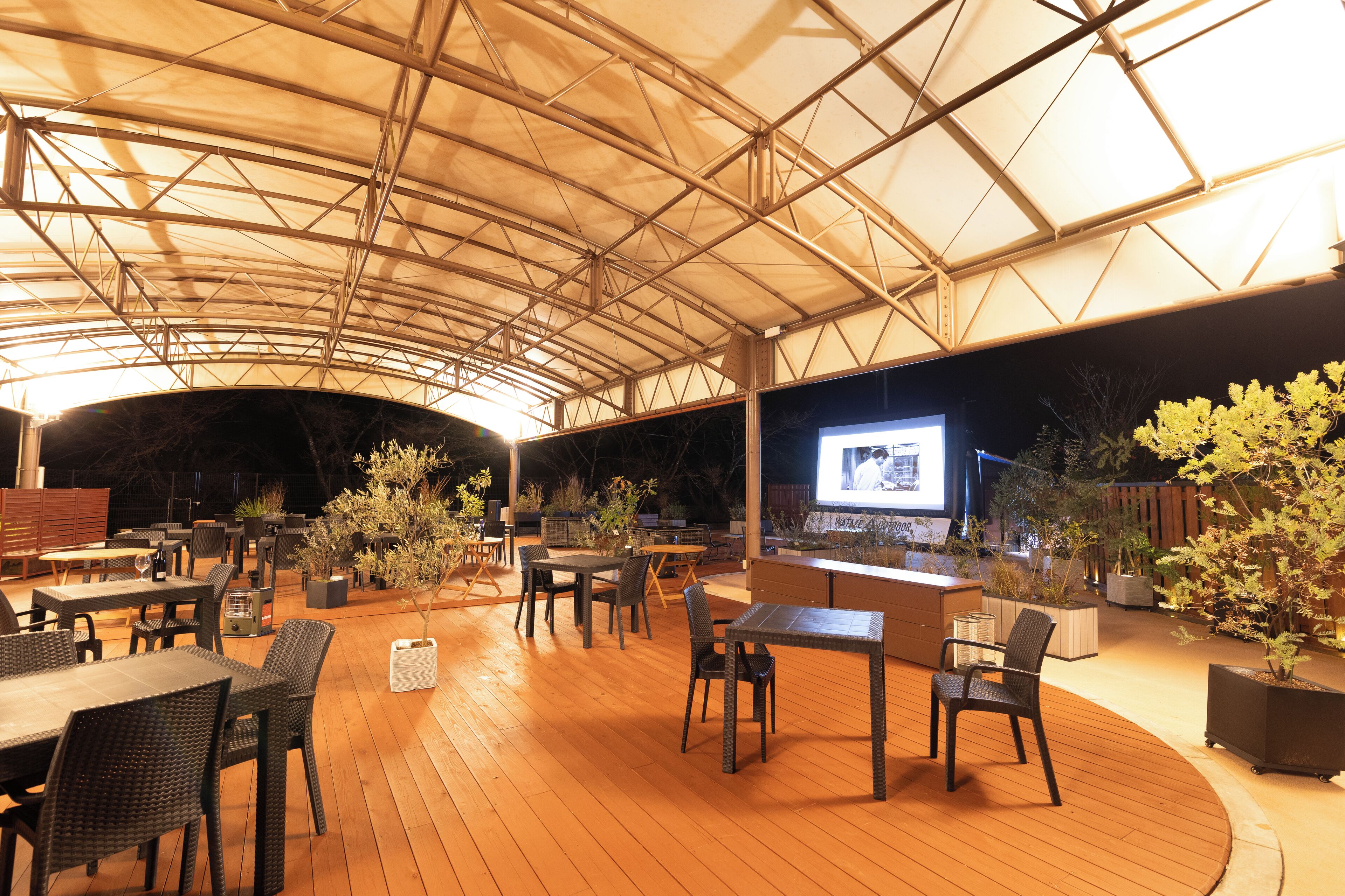 Eine Außenpatio-Terrasse mit Holzboden, Tischen, Stühlen und Blumentöpfen.