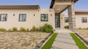 Una casa moderna con techo de tejas, entrada cubierta y camino de acceso pavimentado con borde de piedra.