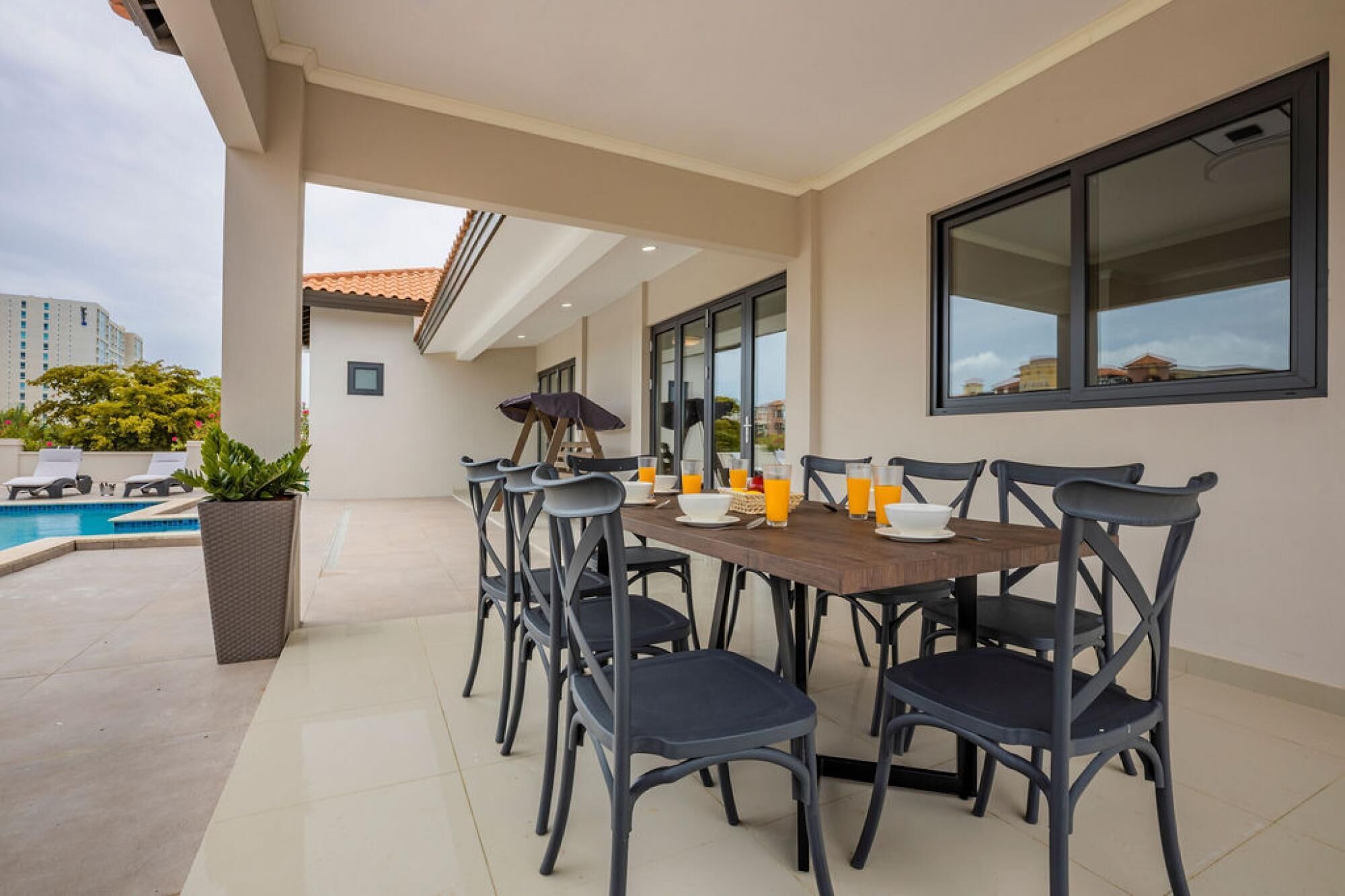 A dining area with a table set for six, surrounded by chairs, near a poolside.