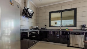 Cocina moderna con armarios negros, lavavajillas de acero inoxidable, pileta doble y un ventanal amplio.