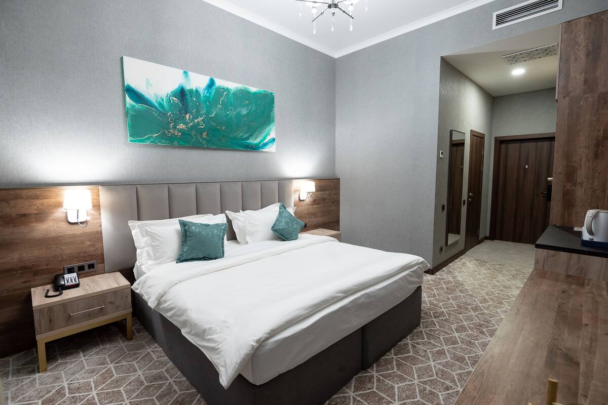 Una habitación de hotel moderna con una cama grande, lámparas de noche, una mesita de noche de madera y un cuadro abstracto colgado en la pared.
