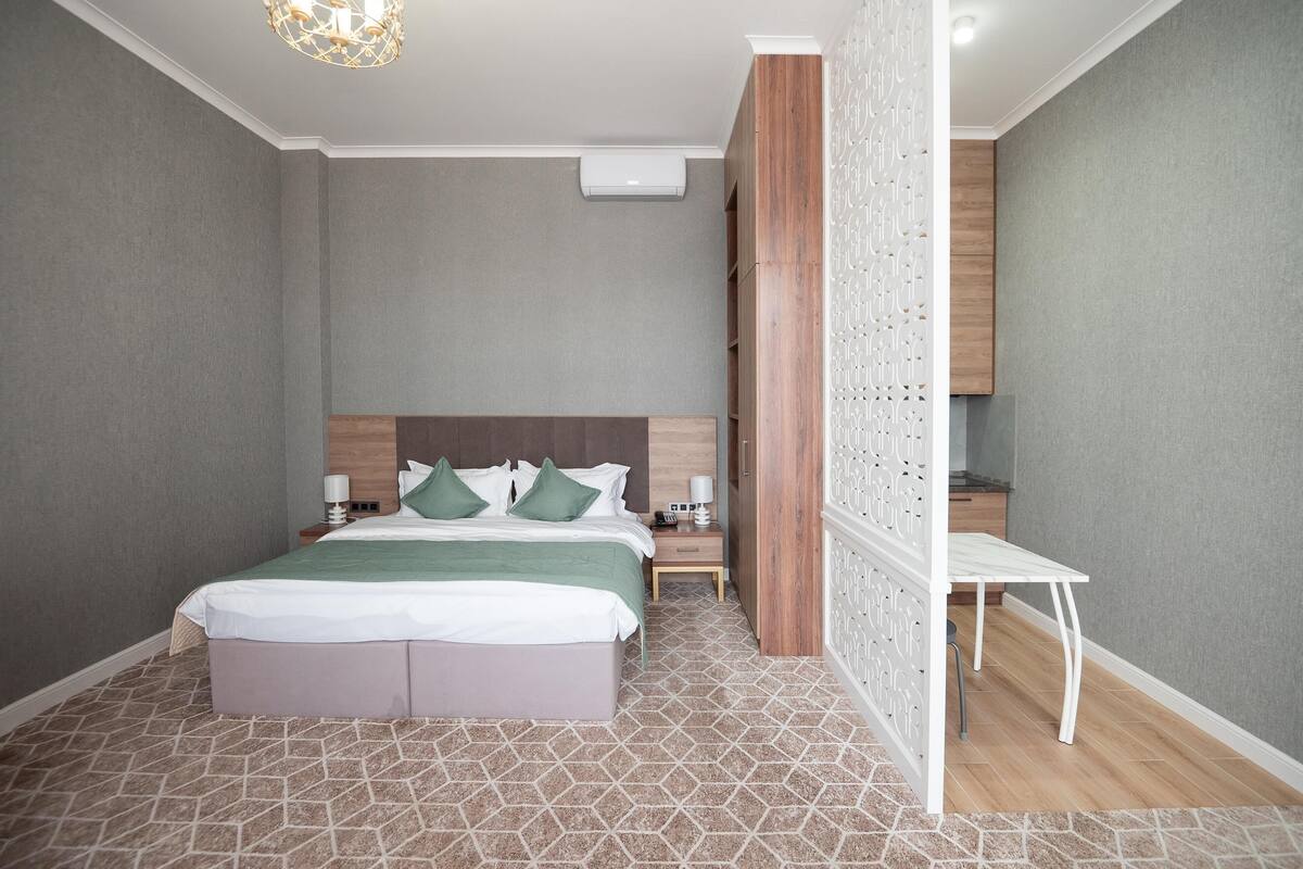 Una habitación de hotel moderna con una cama grande, una mesita de noche, un escritorio pequeño y un panel decorativo en la pared.