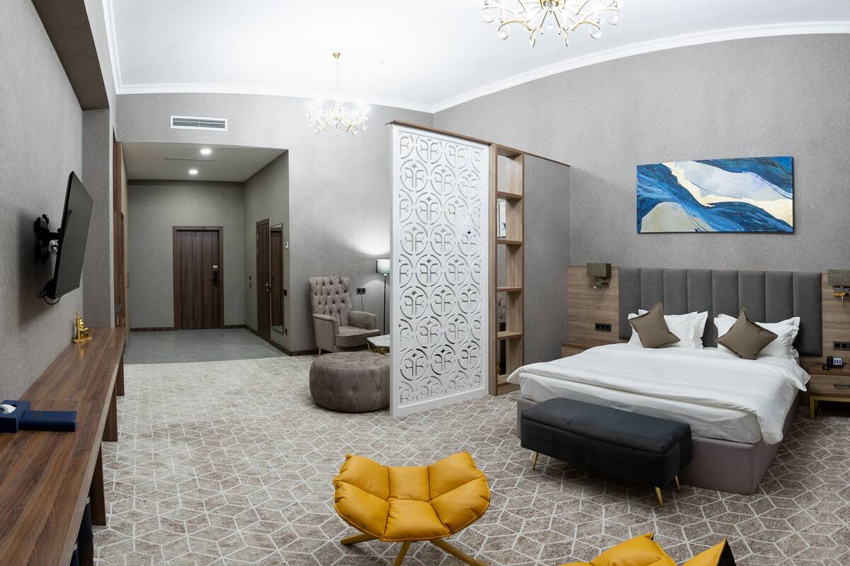 Una habitación de hotel moderna con una cama grande, mesitas de noche, televisión, escritorio, silla y un adorno en la pared.