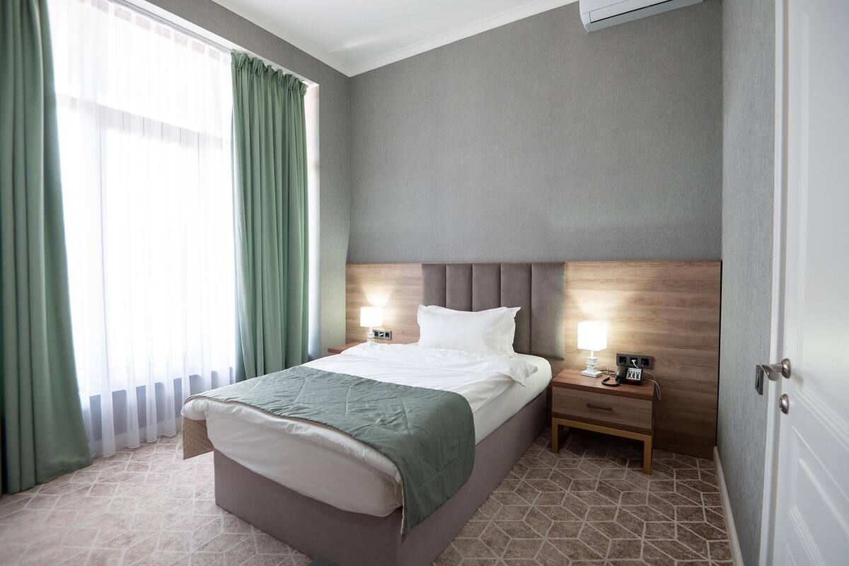 Una habitación de hotel con una cama, lámparas de noche, una mesita de noche y una ventana con cortinas.