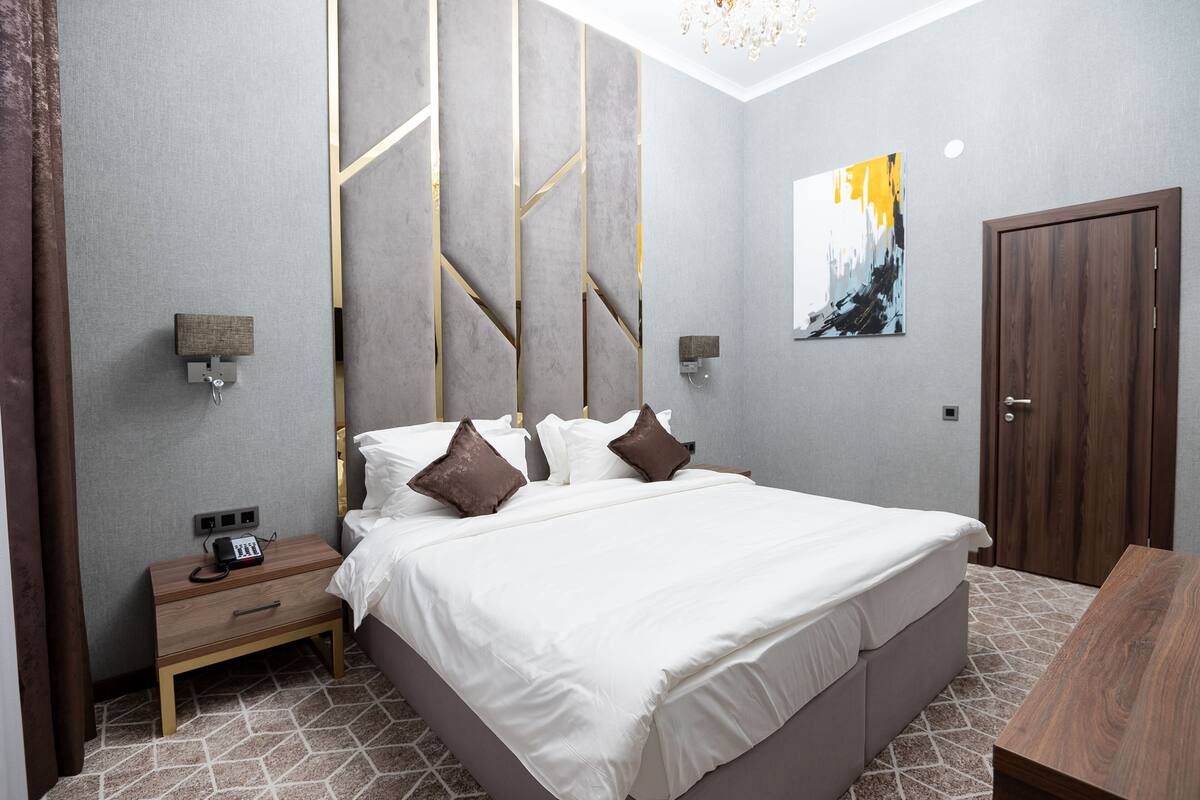 Un dormitorio moderno con una cama grande, mesitas de noche, un tocador y un aparador de madera, junto a una puerta de madera.