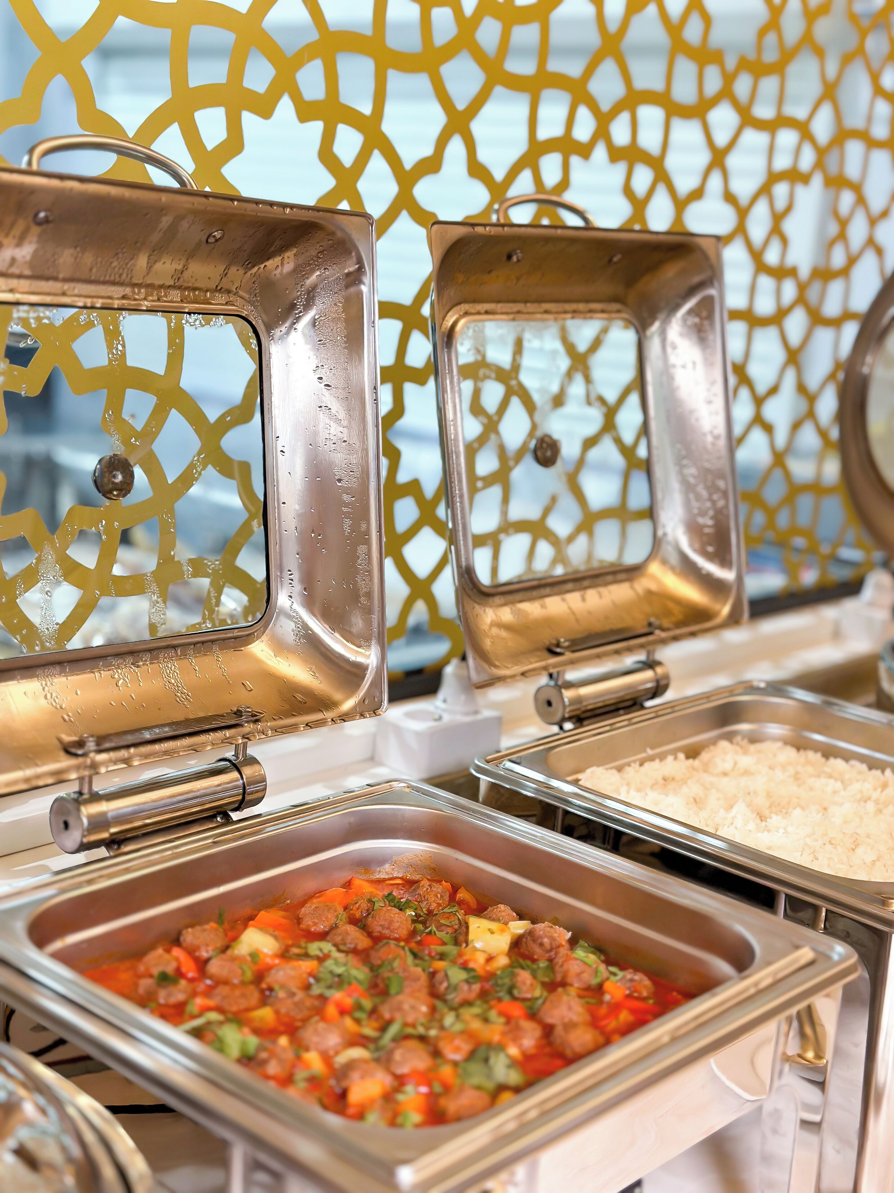A buffet setup with various food items including meatballs, rice, and a vegetable dish.