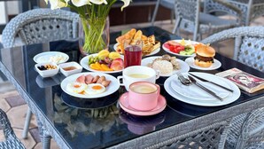 Una mesa de desayuno con diversos platos, un jarrón de flores y asientos al aire libre.