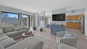 A spacious living area with a sofa set, a coffee table, and a TV mounted on the wall.
