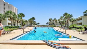 A swimming pool with lounge chairs and palm trees, surrounded by buildings.