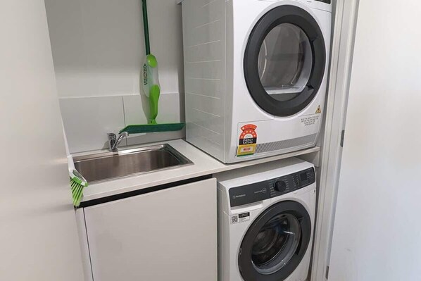 A compact laundry area with a washing machine, a dryer, and a sink. - Modern Torquay Living (Torquay)
