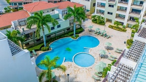 A resort with a central swimming pool, multiple lounge areas, and palm trees.