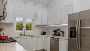Una cucina moderna con mobili bianchi, elettrodomestici in acciaio inossidabile e una finestra che lascia entrare luce naturale.