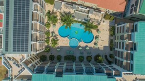 Vista aérea de un hotel con piscina central rodeada de palmeras y tumbonas.