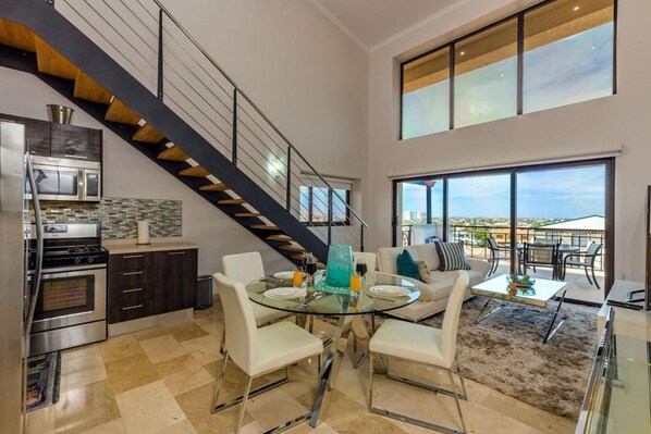 Una cocina moderna con una mesa de comedor de vidrio, sillas blancas y una escalera.