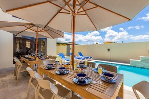 Un espace de restauration en plein air avec vue sur la piscine, des tables en bois et des bols à motifs bleus.