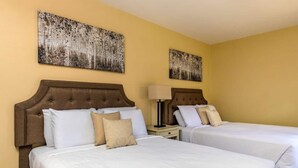 Une chambre d’hôtel avec deux lits, chacun doté d’une tête de lit marron, de draps blancs et d’oreillers beige. Deux tableaux sont accrochés au mur au-dessus des lits.