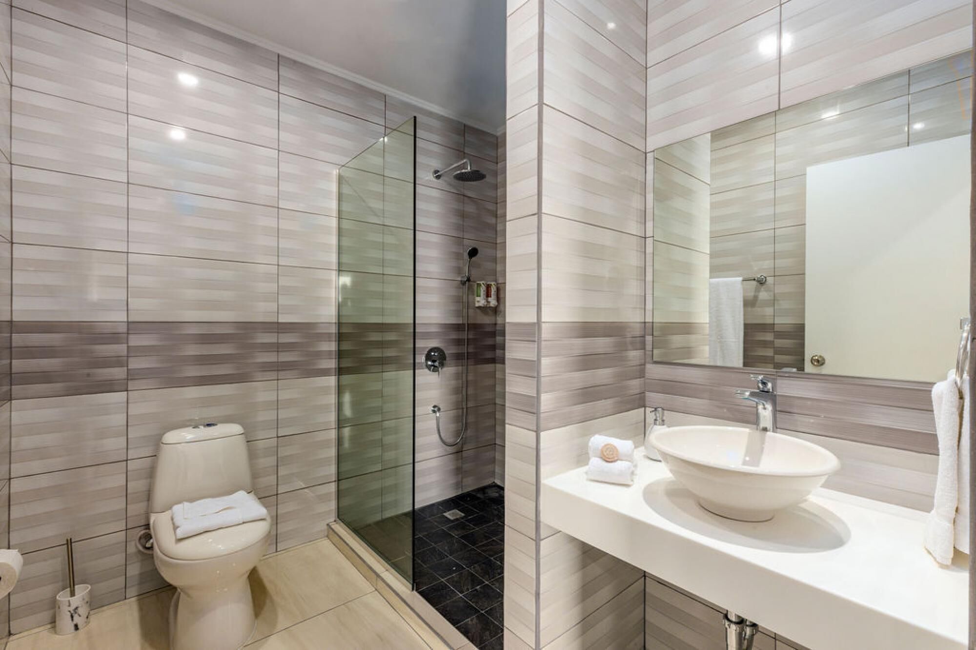 Un baño moderno con cabina de ducha de vidrio, inodoro y lavabo con un espejo grande.