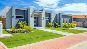 A modern two-story house with a grey exterior, a well-maintained lawn, and a brick pathway leading to the entrance. - NEW 3BR 3BA Villa w Modern Decor and Private Pool (Noord)