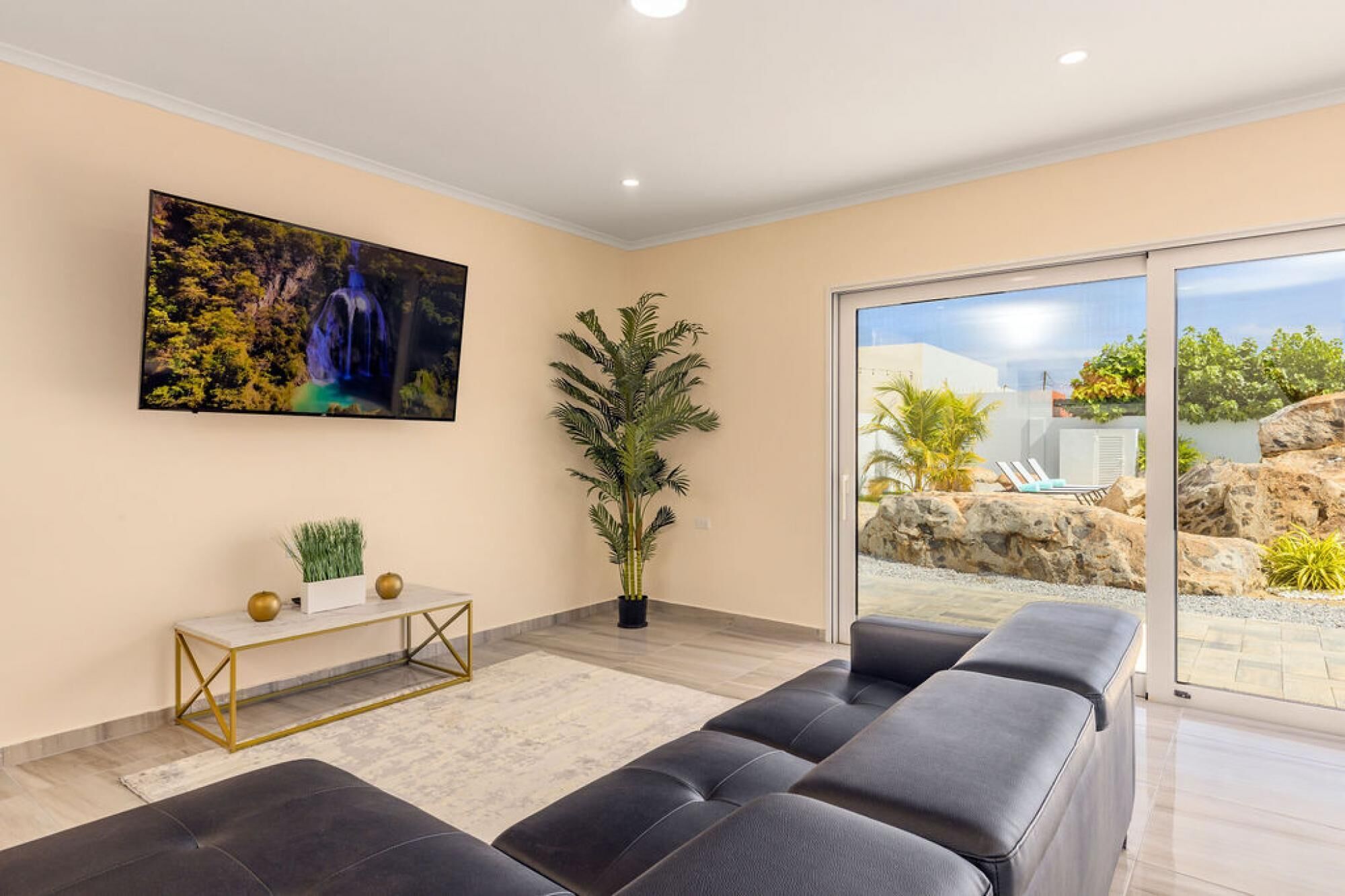 A modern living room with a large TV, a sofa, a small table, and a potted plant.