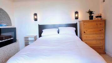 A neatly made bed with white linens, a wooden dresser with drawers, and two wall-mounted sconces.