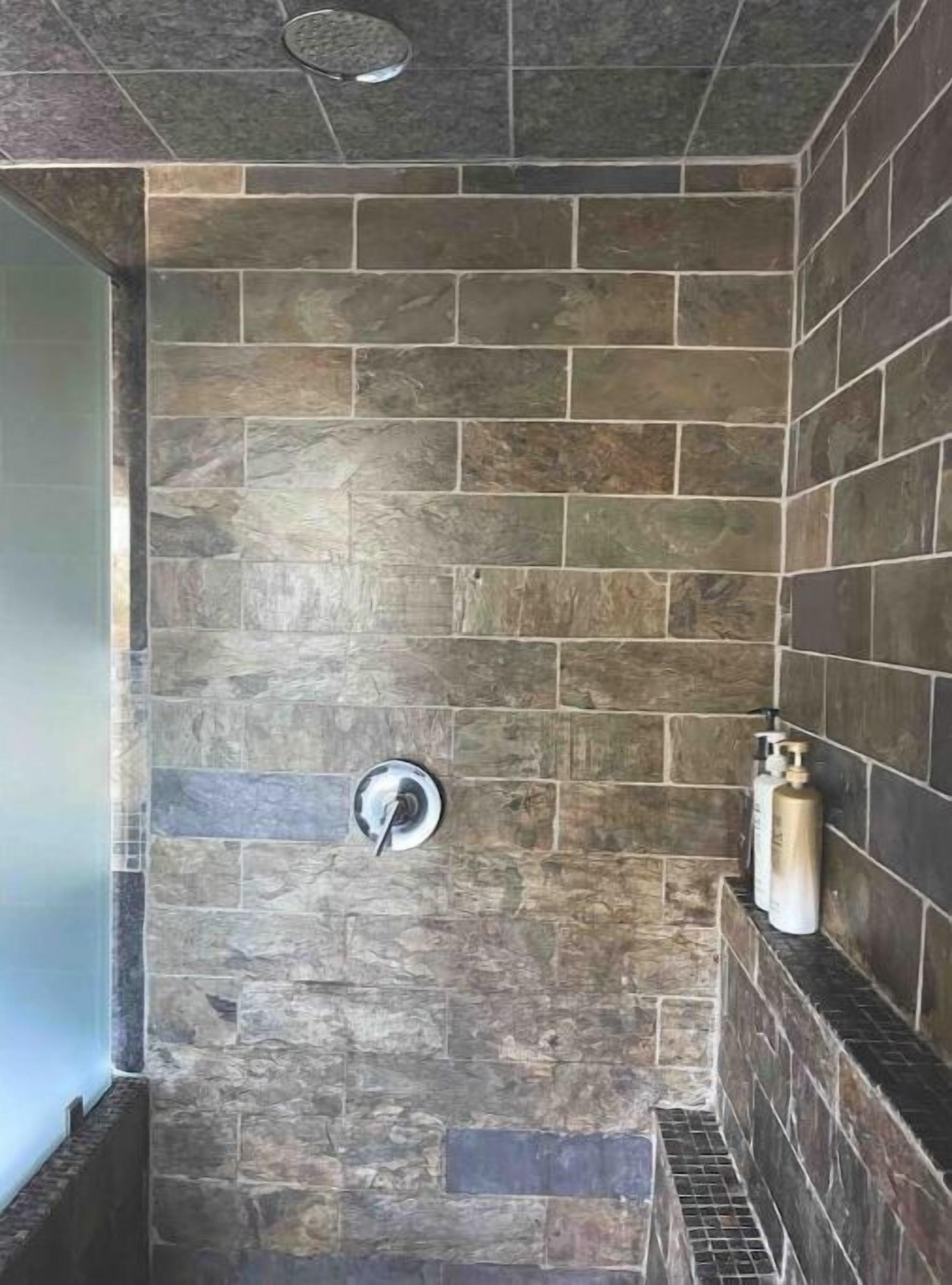 Un espace douche avec des murs en pierre et une pomme de douche en métal.