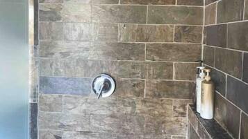 Un espace douche avec des murs en pierre et une pomme de douche en métal.