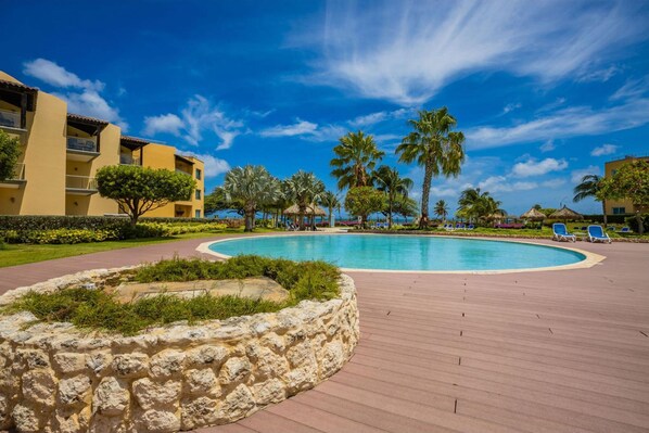Relax by the resort's central pool, surrounded by lush tropical vegetation and a building with balconies.