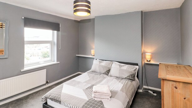 Un dormitorio con cama, ventana, radiador, armario de madera y lámpara colgante.