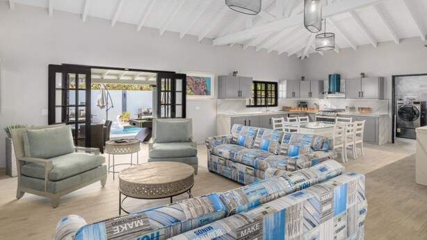 Ein geräumiges Wohnzimmer mit einer Couch, Sesseln und einem Couchtisch. Im Hintergrund ist eine Küche mit modernen Geräten und Schränken zu sehen.