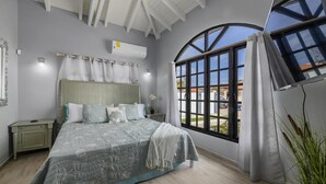 Ein Schlafzimmer mit einem Bett, einem Nachttisch, einem Fenster mit Vorhängen und einer Klimaanlage.
