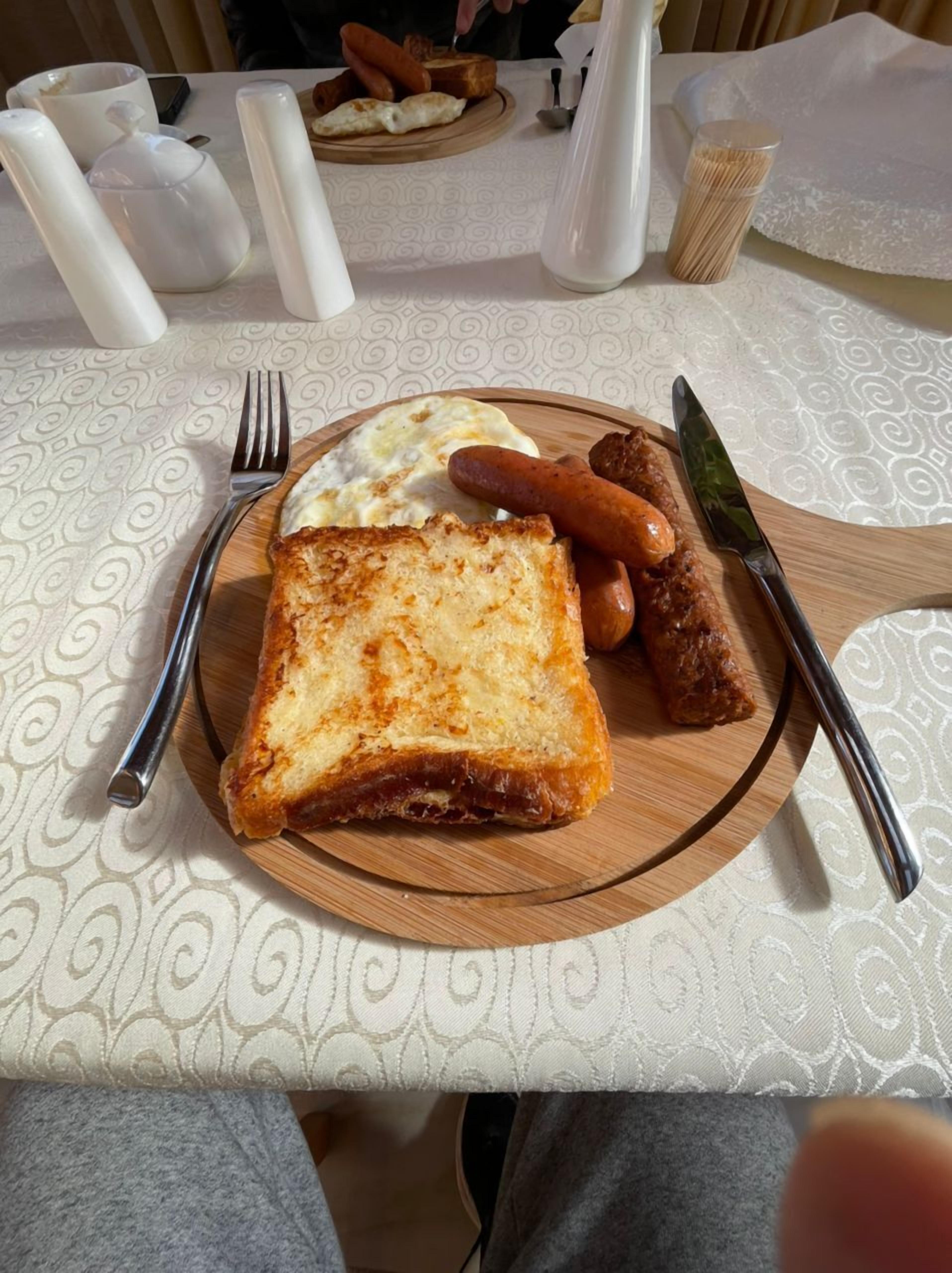 A breakfast plate with toast, sausages, and scrambled eggs on a wooden board.