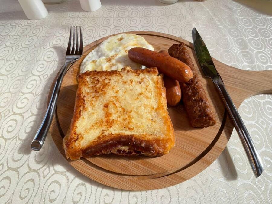 A breakfast plate with toast, sausages, and scrambled eggs on a wooden board.