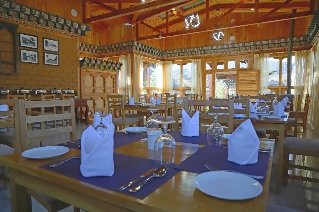 A restaurant with wooden interiors, tables set with white tablecloths, and a high ceiling.