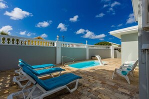 A pool area with lounge chairs and a clear blue sky.