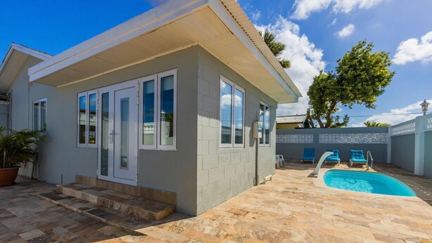 A modern house with a swimming pool, stone patio, and blue lounge chairs. - 3BR Home w Pool in Downtown 5min Walk 2 Beach (Oranjestad)