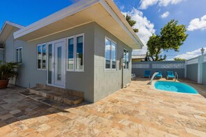 A modern house with a swimming pool, stone patio, and blue lounge chairs.