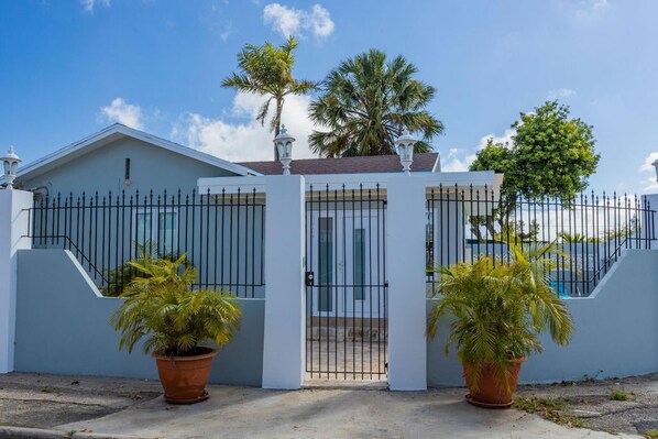 A modern house with a white exterior, a gated entrance, and two potted palm trees in front.