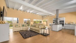 Amplia sala de estar con un sofá color beige, una mesa de centro y una alfombra. Se observa una cocina con electrodomésticos modernos y una isla grande.