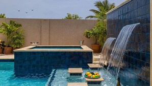 Una piscina con cascada, rodeada de plantas en macetas y un cielo despejado.