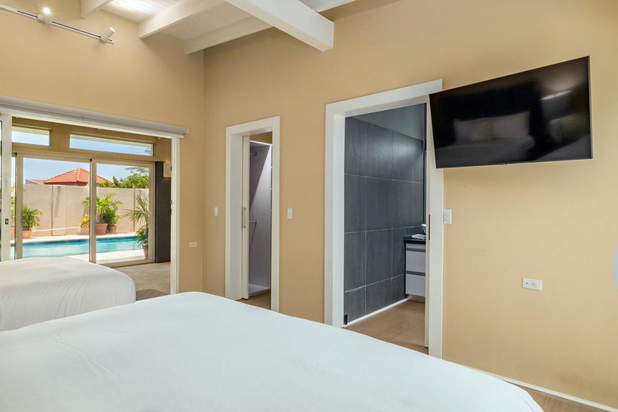 A hotel room with a bed, a TV mounted on the wall, and a view of a swimming pool outside.