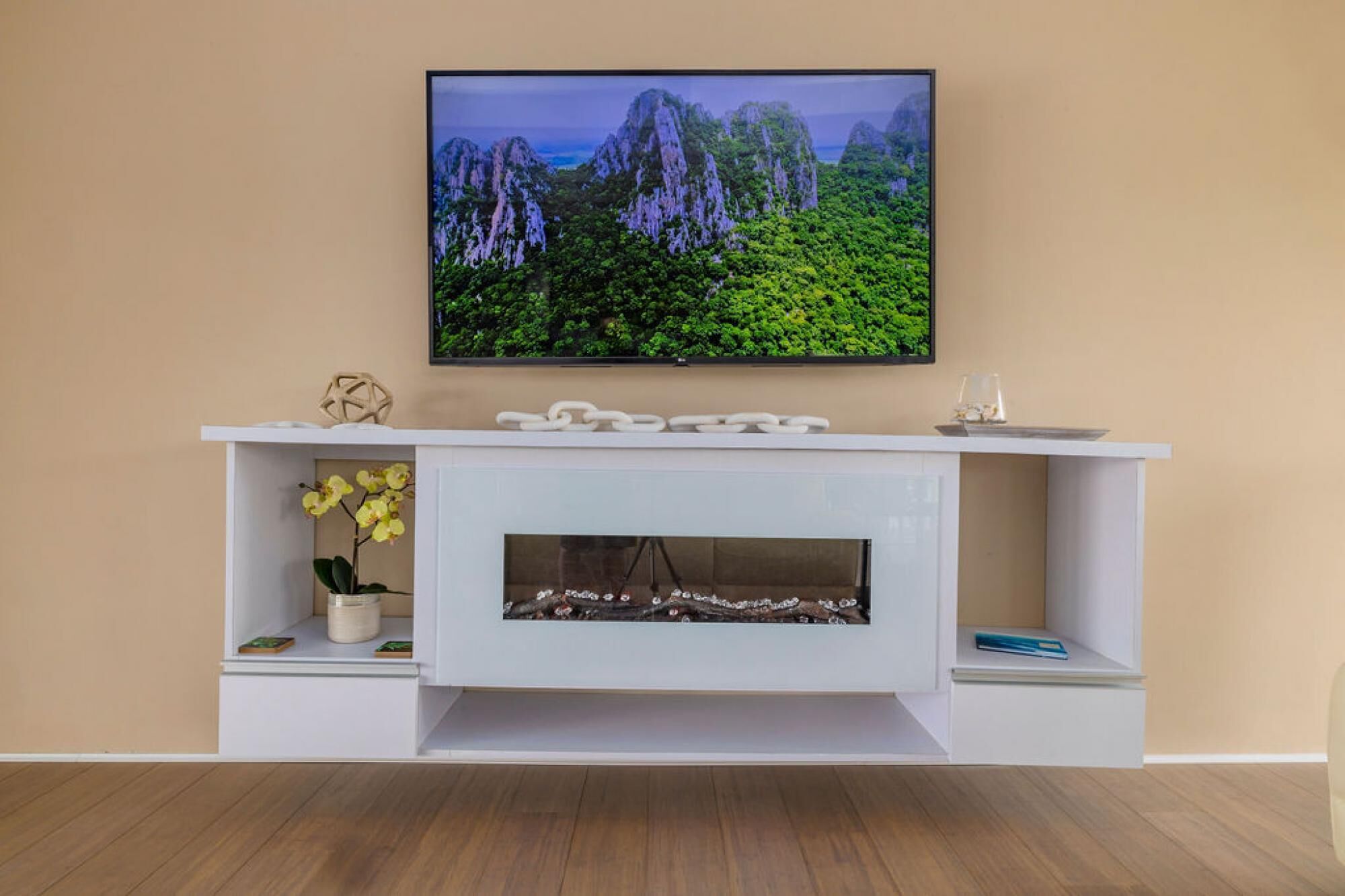 A modern living room with a white entertainment unit, a flat-screen TV mounted above it, and a fireplace below.