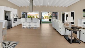 Una cocina moderna con armarios blancos, electrodomésticos de acero inoxidable y un comedor con sillas blancas.