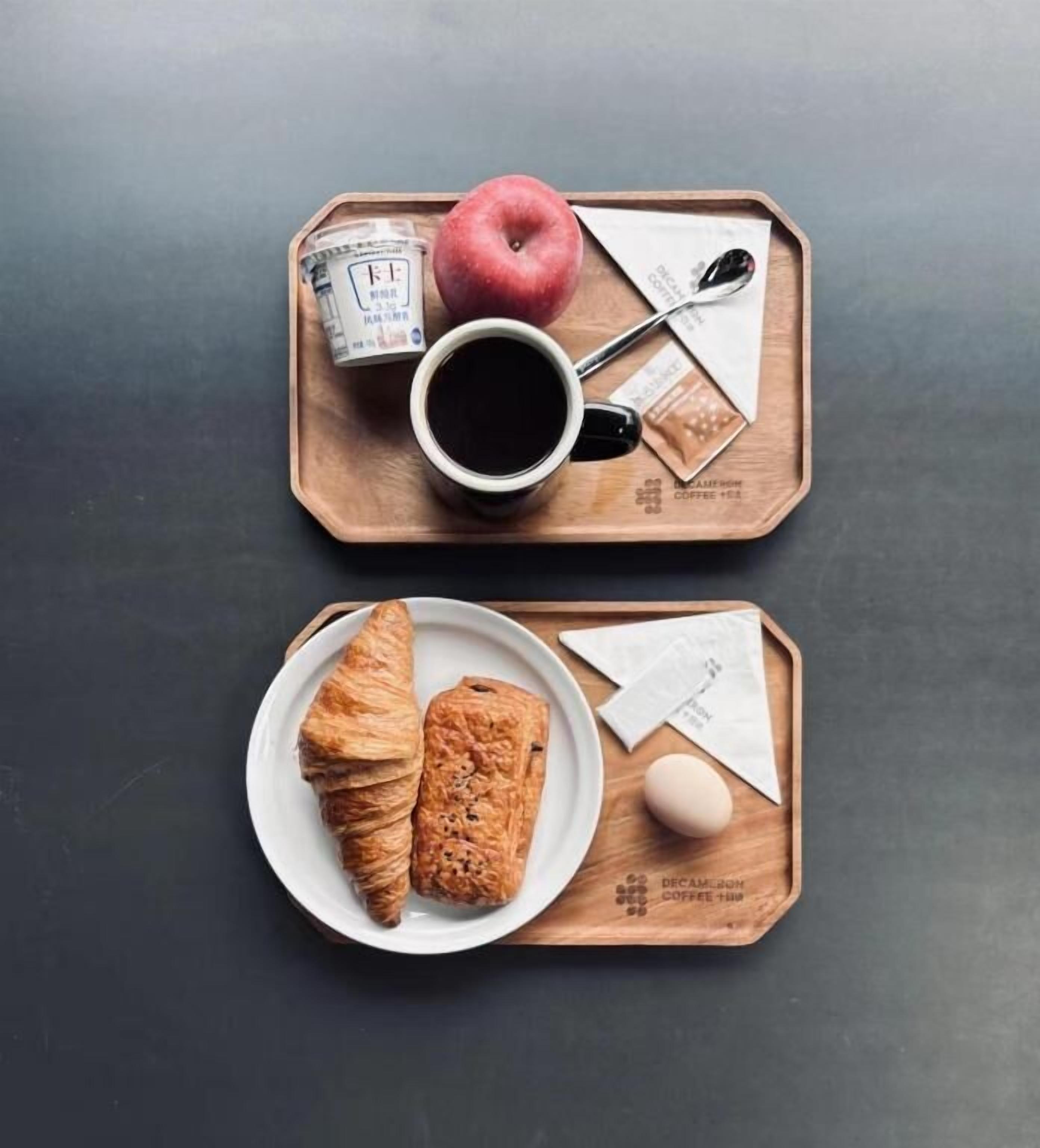 A tray with a red apple, a cup of coffee, and two pastries on a dark surface.