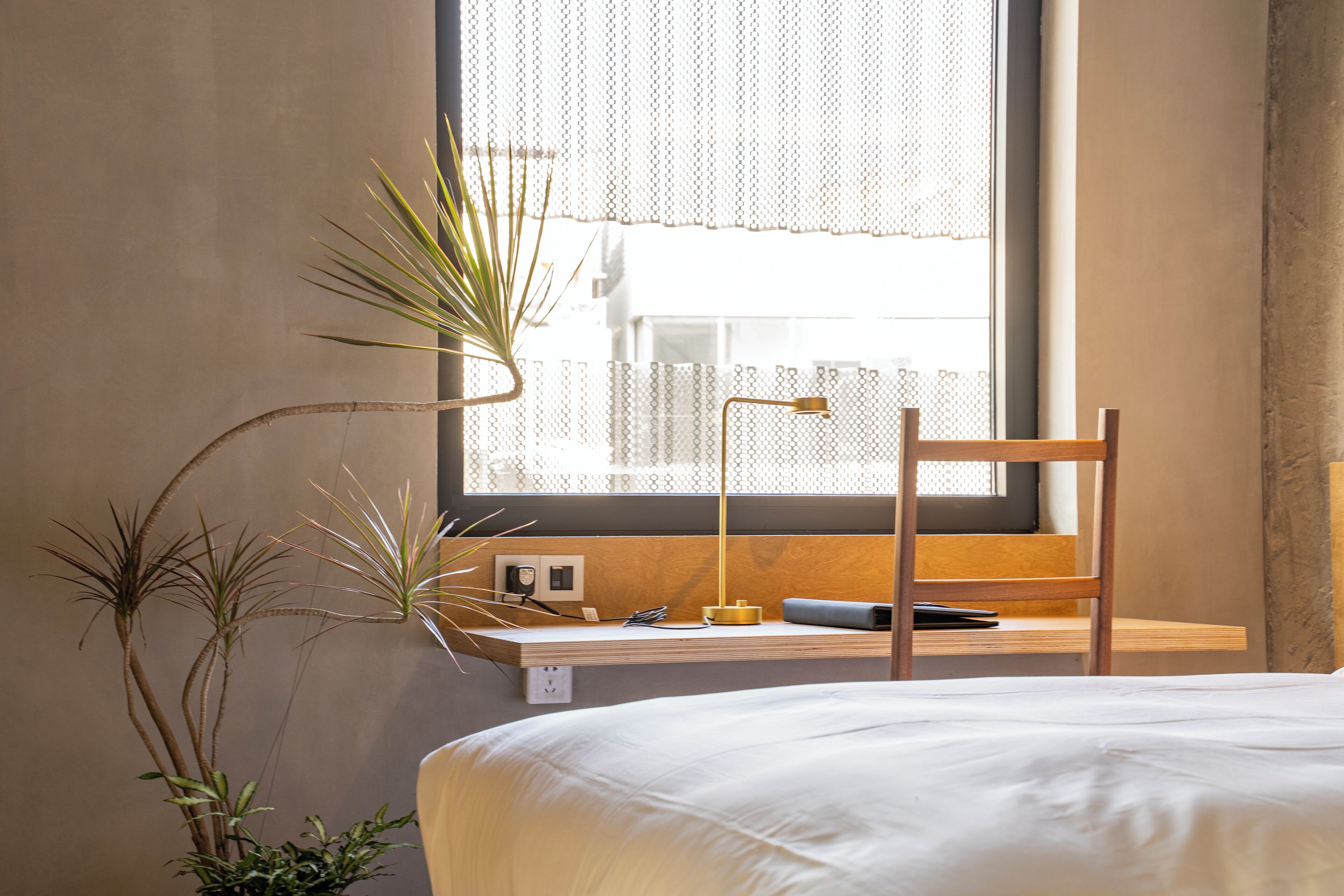 Ein Schlafzimmer mit Bett, Schreibtisch mit Lampe und einem Fenster mit Blick auf Gebäude.